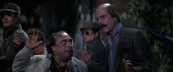 Movie still from “Romancing the Stone” (1984), directed by Robert Zemeckis – A man with a beard is talking to another man in a suit; Medium shot, Over the shoulder angle