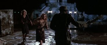 Movie still from “Romancing the Stone” (1984), directed by Robert Zemeckis – A woman in a brown dress and a man in a brown jacket; Wide shot, Over the shoulder angle