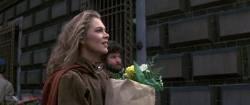 Movie still from “Romancing the Stone” (1984), directed by Robert Zemeckis – A woman holding a paper bag with flowers in it; Close Up shot, Over the shoulder angle