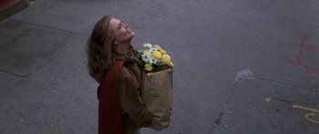 Movie still from “Romancing the Stone” (1984), directed by Robert Zemeckis – A woman holding a bag of flowers on the street; Medium shot, Overhead angle