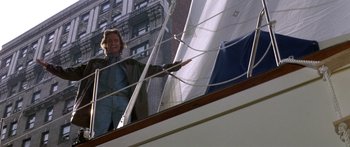 Movie still from “Romancing the Stone” (1984), directed by Robert Zemeckis – A man standing on the side of a boat in the water; Wide shot, Low angle