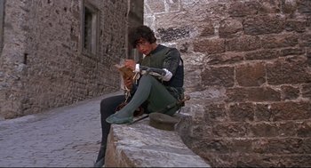 Movie still from “Romeo and Juliet” (1968), directed by Franco Zeffirelli – A man sitting on a stone wall while holding a guitar; Wide shot, High angle