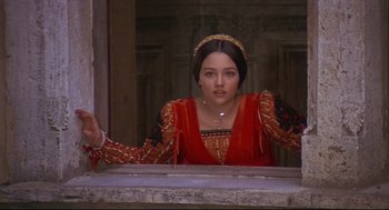 Movie still from “Romeo and Juliet” (1968), directed by Franco Zeffirelli – A woman in a red dress is standing in front of a window; Medium shot, Over the shoulder angle