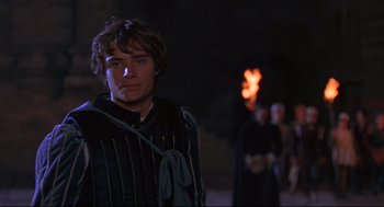 Movie still from “Romeo and Juliet” (1968), directed by Franco Zeffirelli – A young man in medieval garb standing in front of a fire; Medium shot, Over the shoulder angle