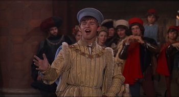Movie still from “Romeo and Juliet” (1968), directed by Franco Zeffirelli – A man wearing a blue hat and a gold dress; Medium shot, High angle