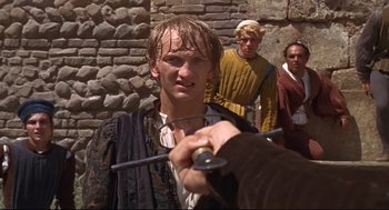 Movie still from “Romeo and Juliet” (1968), directed by Franco Zeffirelli – A man holding a sword in front of two other men; Close Up shot, Over the shoulder angle