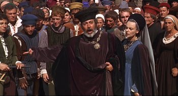 Movie still from “Romeo and Juliet” (1968), directed by Franco Zeffirelli – A crowd of people are gathered around a man wearing a crown; Medium shot, High angle