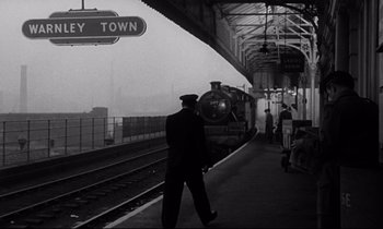 Movie still from “Room at the Top” (1958), directed by Jack Clayton – Black and white photograph of a man walking on a train platform; Wide shot, Low angle