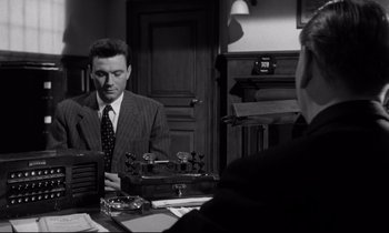 Movie still from “Room at the Top” (1958), directed by Jack Clayton – A man in a suit and tie looking at his watch; Medium shot, Over the shoulder angle