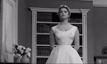Movie still from “Room at the Top” (1958), directed by Jack Clayton – A woman in a white dress standing in front of a bookshelf; Medium shot, Low angle