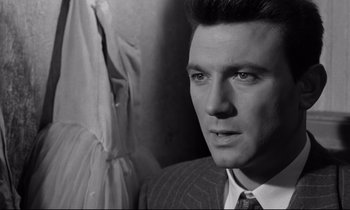 Movie still from “Room at the Top” (1958), directed by Jack Clayton – A black and white photo of a man in a suit and tie; Close Up shot, Over the shoulder angle