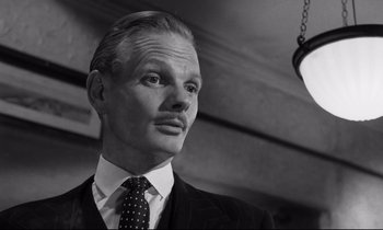 Movie still from “Room at the Top” (1958), directed by Jack Clayton – Black and white photograph of a man in a suit and tie; Close Up shot, Low angle