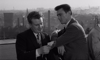Movie still from “Room at the Top” (1958), directed by Jack Clayton – Two men in suits are looking at a piece of paper; Medium shot, High angle