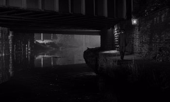 Movie still from “Room at the Top” (1958), directed by Jack Clayton – A man standing next to a body of water under a bridge; Extreme Wide shot, High angle