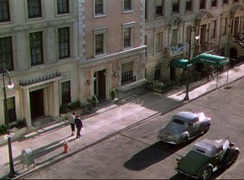 Movie still from “Rope” (1948), directed by Alfred Hitchcock – Two people walking down the sidewalk of a street in front of a building; Extreme Wide shot, High angle