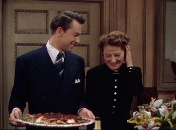 Movie still from “Rope” (1948), directed by Alfred Hitchcock – A man and a woman standing in front of a cake; Medium shot, Over the shoulder angle