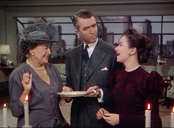 Movie still from “Rope” (1948), directed by Alfred Hitchcock – Two women and a man standing in front of candles; Medium shot, Over the shoulder angle
