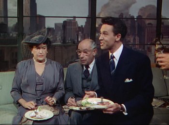 Movie still from “Rope” (1948), directed by Alfred Hitchcock – A man and a woman sitting next to a man holding a plate of food; Medium shot, Over the shoulder angle