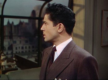 Movie still from “Rope” (1948), directed by Alfred Hitchcock – A man wearing a suit and tie standing in front of a window; Medium shot, Over the shoulder angle