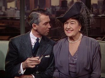 Movie still from “Rope” (1948), directed by Alfred Hitchcock – An older man standing next to an older woman holding a glass; Medium shot, High angle