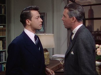 Movie still from “Rope” (1948), directed by Alfred Hitchcock – Two men in suits talking to each other in front of a lamp; Medium shot, Over the shoulder angle