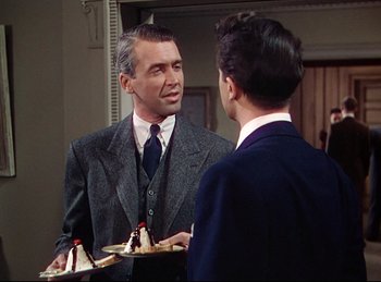 Movie still from “Rope” (1948), directed by Alfred Hitchcock – A man in a suit and tie talking to another man in a suit and tie in front of a mirror; Medium shot, Over the shoulder angle