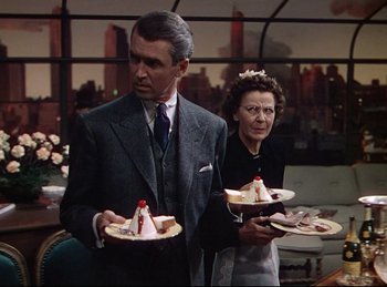 Movie still from “Rope” (1948), directed by Alfred Hitchcock – A man and a woman standing next to each other holding plates; Medium shot, Over the shoulder angle