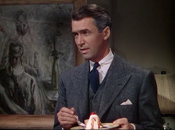 Movie still from “Rope” (1948), directed by Alfred Hitchcock – A man in a suit and tie eating a piece of cake; Medium shot, Over the shoulder angle