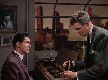 Movie still from “Rope” (1948), directed by Alfred Hitchcock – A man in a suit and tie holding a bottle of beer; Medium shot, Low angle