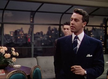 Movie still from “Rope” (1948), directed by Alfred Hitchcock – A man in a suit and tie standing in front of another man; Medium shot, Over the shoulder angle