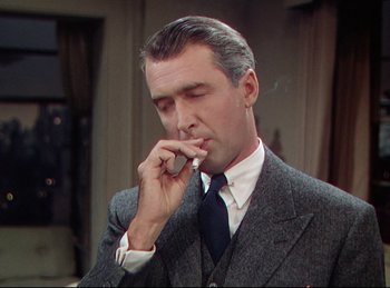Movie still from “Rope” (1948), directed by Alfred Hitchcock – A man in a suit and tie smoking a cigarette; Close Up shot, Low angle