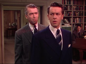 Movie still from “Rope” (1948), directed by Alfred Hitchcock – A man in a suit and tie standing next to another man in a suit and tie; Medium shot, Over the shoulder angle