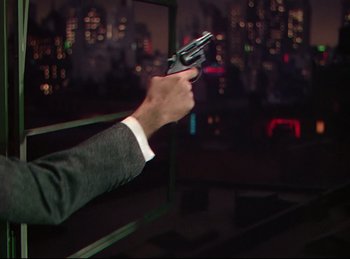 Movie still from “Rope” (1948), directed by Alfred Hitchcock – A man in a suit holding a gun in his right hand; Close Up shot, High angle