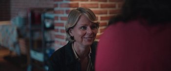 Movie still from “Rose” (2022), directed by Niels Arden Oplev – A person smiling at a table; Close Up shot, Over the shoulder angle