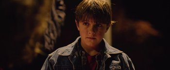 Movie still from “Rose” (2022), directed by Niels Arden Oplev – A young boy wearing a jean jacket looking at the camera; Close Up shot, Over the shoulder angle