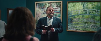 Movie still from “Rose” (2022), directed by Niels Arden Oplev – A man in a suit holding an open book in his hands; Medium shot, Over the shoulder angle