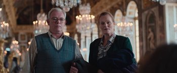 Movie still from “Rose” (2022), directed by Niels Arden Oplev – A man and a woman standing next to each other in front of chandeliers; Medium shot, Low angle