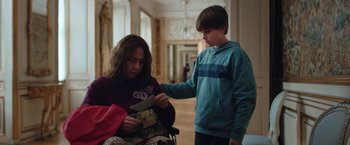 Movie still from “Rose” (2022), directed by Niels Arden Oplev – A woman sitting in a chair next to a young boy; Medium shot, Over the shoulder angle