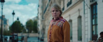 Movie still from “Rose” (2022), directed by Niels Arden Oplev – A woman standing in front of a tall building; Medium shot, Low angle