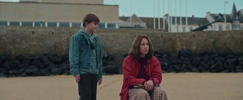 Movie still from “Rose” (2022), directed by Niels Arden Oplev – A woman and a boy sitting on a beach; Medium shot, Over the shoulder angle