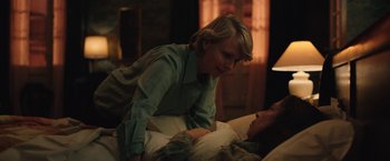 Movie still from “Rose” (2022), directed by Niels Arden Oplev – A woman sitting next to a man laying on a bed; Medium shot, Over the shoulder angle