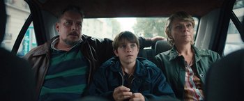Movie still from “Rose” (2022), directed by Niels Arden Oplev – Three people sitting in the back of a car; Medium shot, Low angle