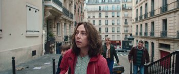 Movie still from “Rose” (2022), directed by Niels Arden Oplev – A woman is walking down the street in a red jacket; Medium shot, High angle