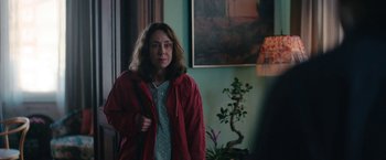 Movie still from “Rose” (2022), directed by Niels Arden Oplev – A woman wearing a red jacket standing in front of a painting; Medium shot, Over the shoulder angle