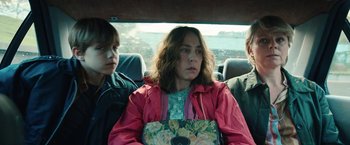 Movie still from “Rose” (2022), directed by Niels Arden Oplev – A woman sitting in the back of a car next to two other people; Medium shot, High angle