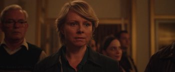 Movie still from “Rose” (2022), directed by Niels Arden Oplev – A woman with blonde hair is standing in front of other people; Close Up shot, Over the shoulder angle