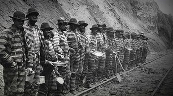 Movie still from “13th” (2016), directed by Ava DuVernay – A black and white photo of a group of men in prison uniforms; Wide shot, High angle