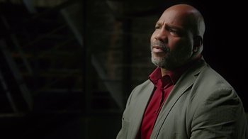Movie still from “13th” (2016), directed by Ava DuVernay – A bald man in a red shirt and a gray suit jacket; Close Up shot, Low angle