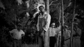 Movie still from “13th” (2016), directed by Ava DuVernay – An old black and white photo of a man standing next to a tree; Wide shot, Low angle