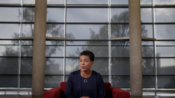 Movie still from “13th” (2016), directed by Ava DuVernay – A woman sitting on a red chair in front of a large window; Medium shot, Low angle